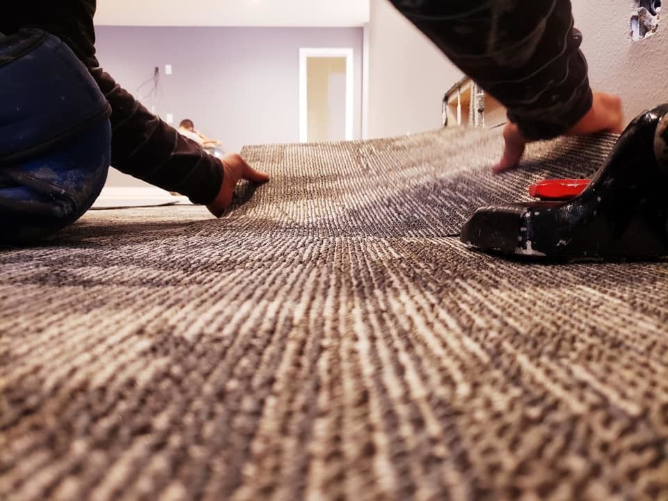 Hands laying carpet in a room, with a roller on the floor.