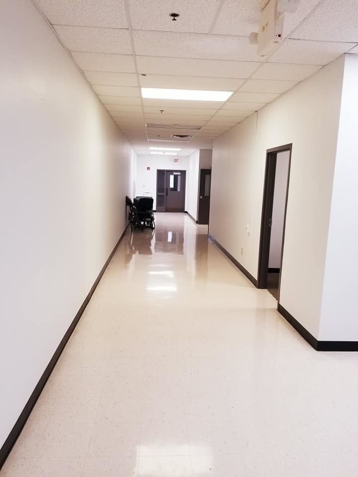 Empty hospital hallway with white walls, glossy floor, and doors on both sides