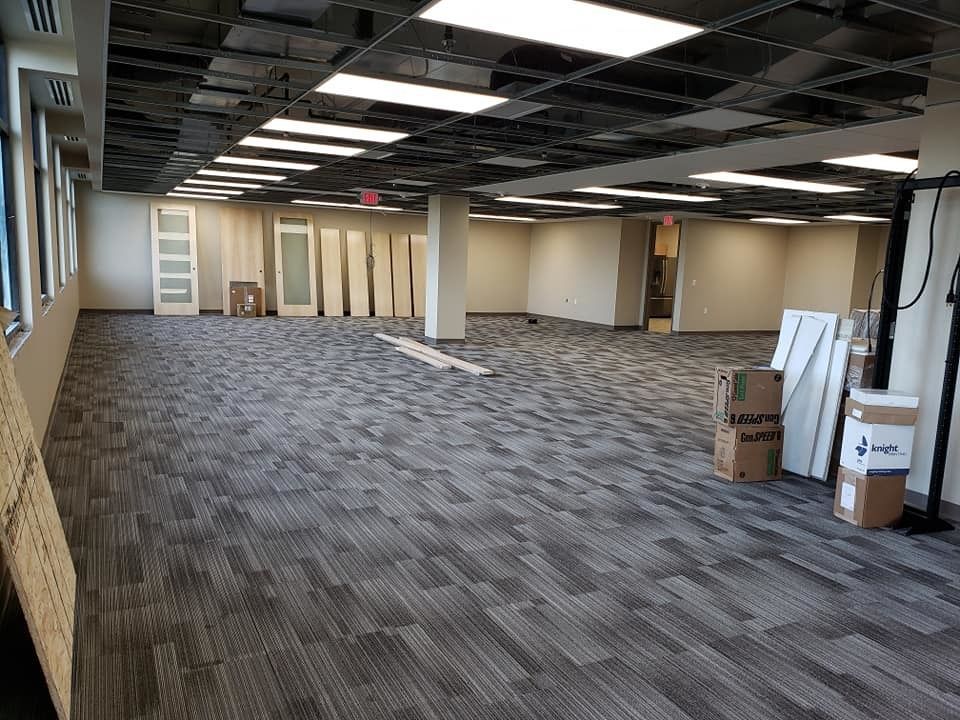 Empty office space with gray carpet, exposed ceiling, columns, and stacked boxes near the wall