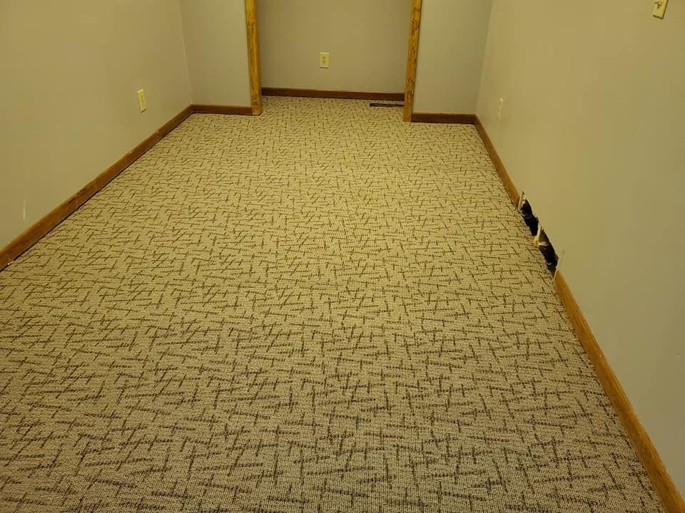 Empty carpeted hallway with beige walls and wooden trim, viewed toward a doorway.