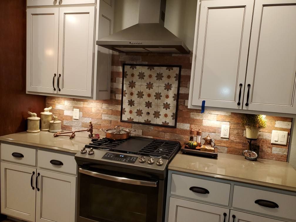 Compact white kitchen with gas range, brick backsplash, under-cabinet lights, and decorative tile behind the stove