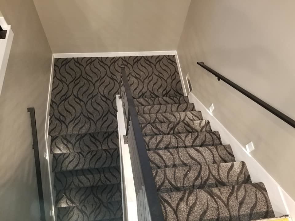 Carpeted stairwell with black handrails and a central divider, viewed from the top landing