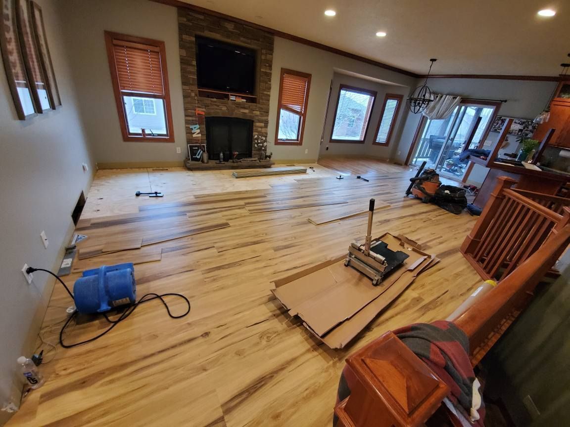 Living room under renovation with new hardwood floor, scattered tools, and furniture along the walls.