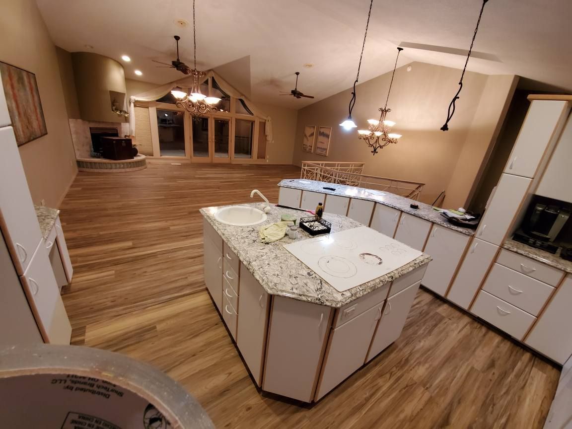 Spacious kitchen with island, white cabinets, wood floors, and pendant lights overlooking an open living area