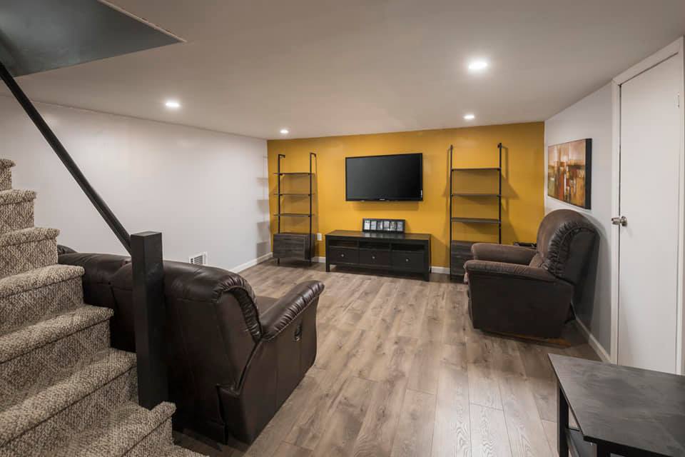 Finished basement with brown reclining chairs, TV on yellow wall, stairs.
