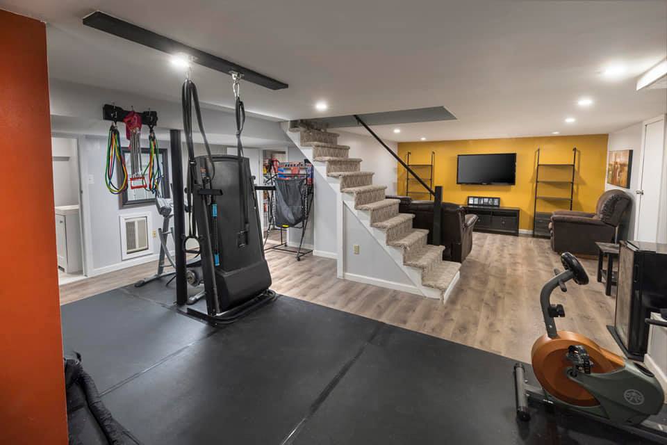 Basement gym with exercise equipment and entertainment area, including a treadmill, bike, and TV.