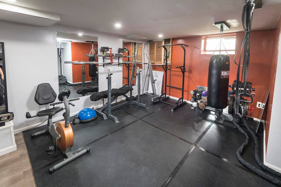 Home gym with workout equipment, black flooring, and red and gray walls.