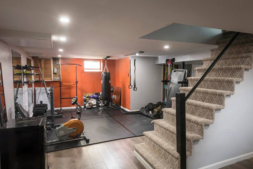 Home gym with workout equipment, orange and gray walls, stairs with carpet.