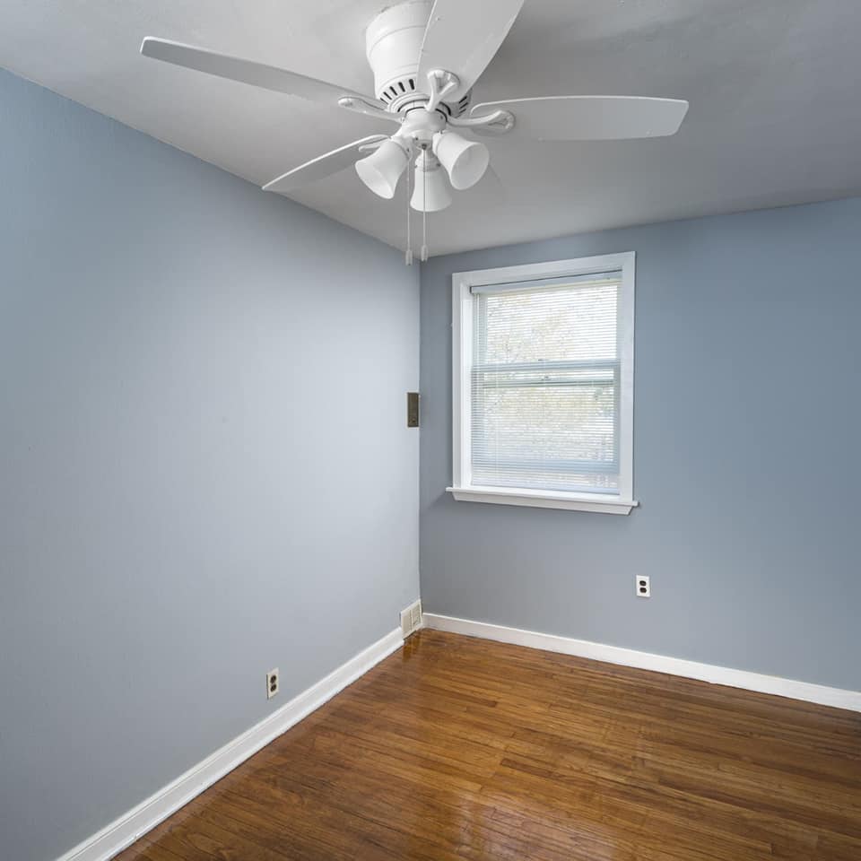 Empty room with blue walls, ceiling fan, window, and hardwood floor.