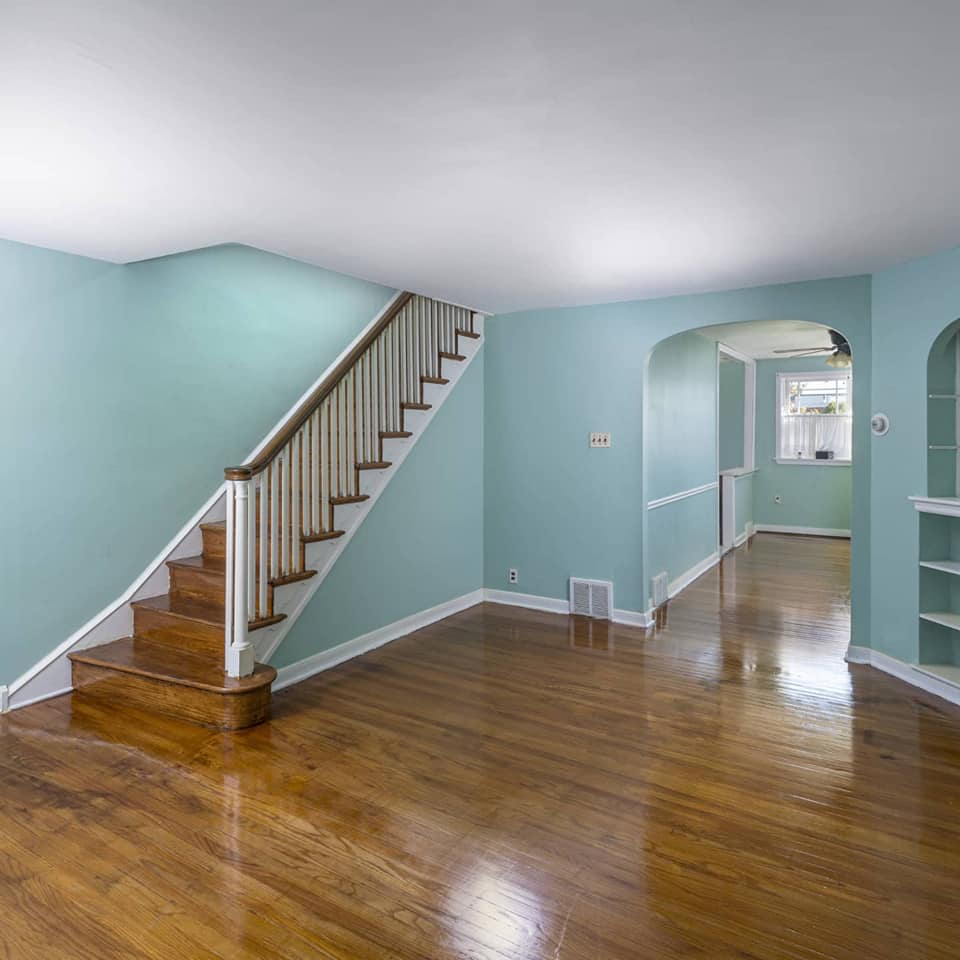 Empty living room with wood floors, stairs, and light blue walls.