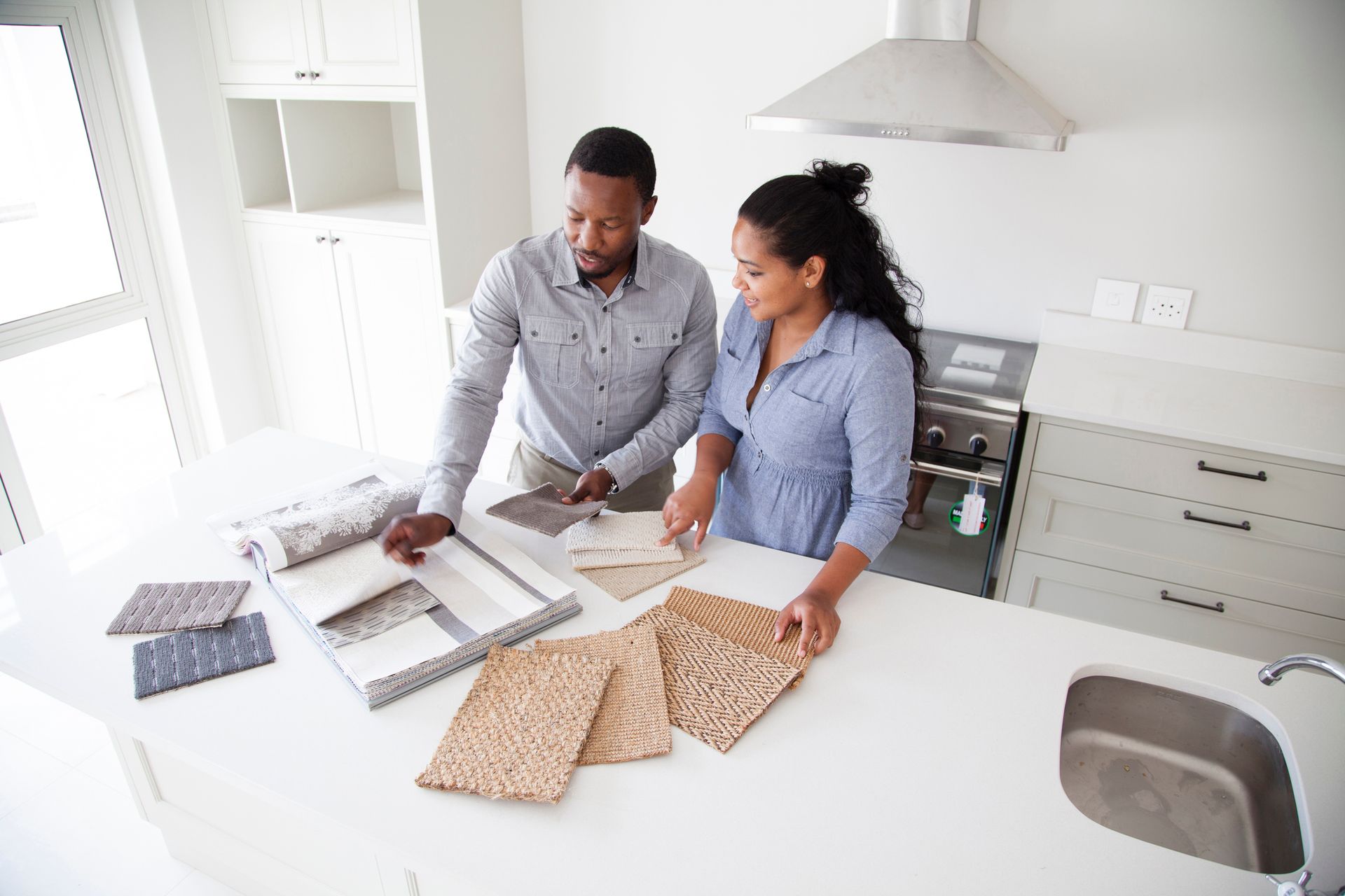 Couple selecting kitchen textures in modern white kitchen with island and design samples.