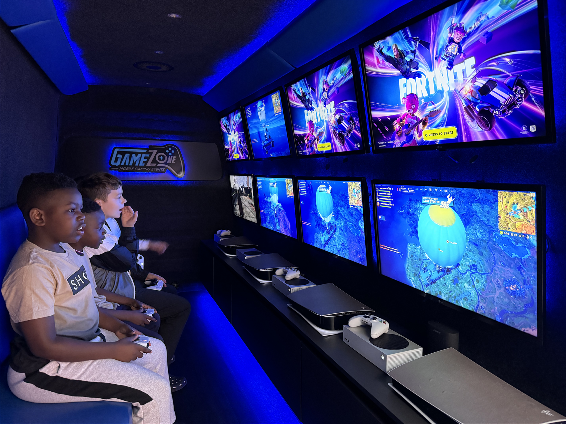 Kids playing video games in a neon-lit arcade with multiple large screens