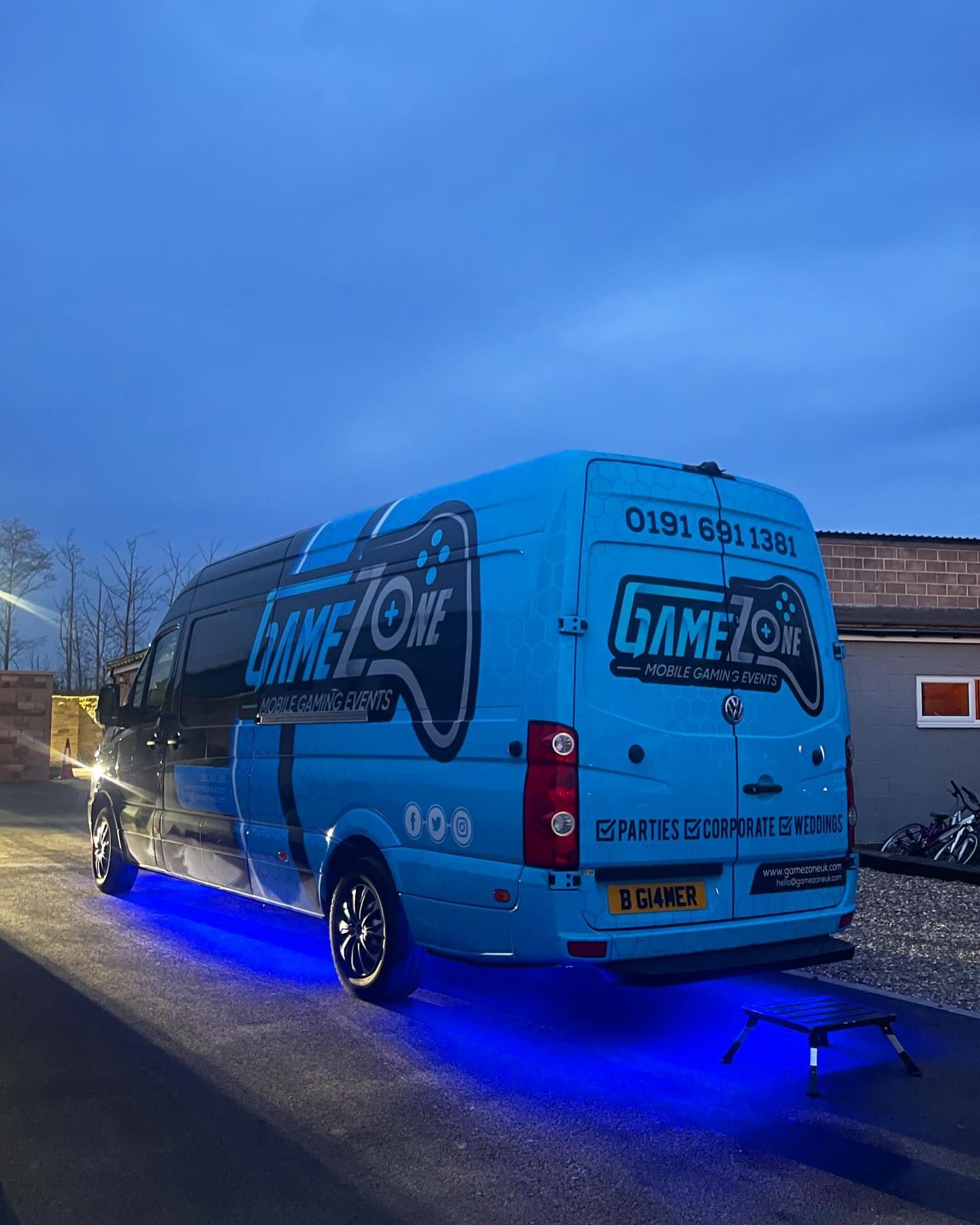 Blue GAME ON van with glowing undercarriage lights parked outdoors at dusk.