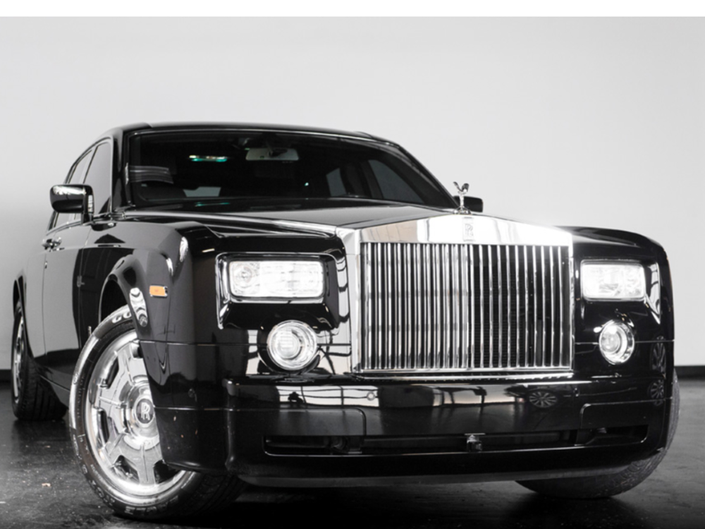 A black rolls royce parked in front of a white wall