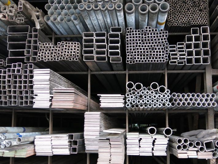Scaffali pieni di tubi e barre metalliche di vario tipo, tra cui rettangolari, quadrate e rotonde.