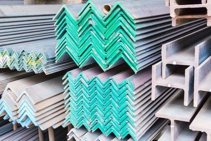 Pile di angolari in acciaio e travi a I in un magazzino, alcune delle quali dipinte di verde.
