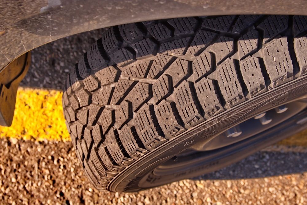 Close-up of a Car Tire With Deep Tread on Gravel Beside a Yellow Road Marking — Mareeba Tyre Centre in Mareeba, QLD