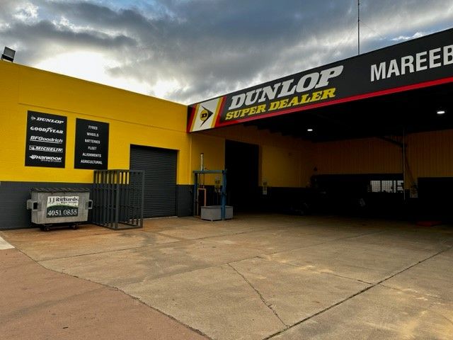 Yellow-and-black Dunlop Tire Shop Exterior With Concrete Forecourt and Cloudy Sky — Mareeba Tyre Centre in Mareeba, QLD