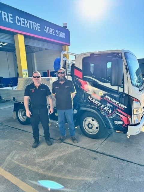 Two Workers Standing Beside a Colourful Delivery Truck Outside a Warehouse Loading Bay — Mareeba Tyre Centre in Mareeba, QLD