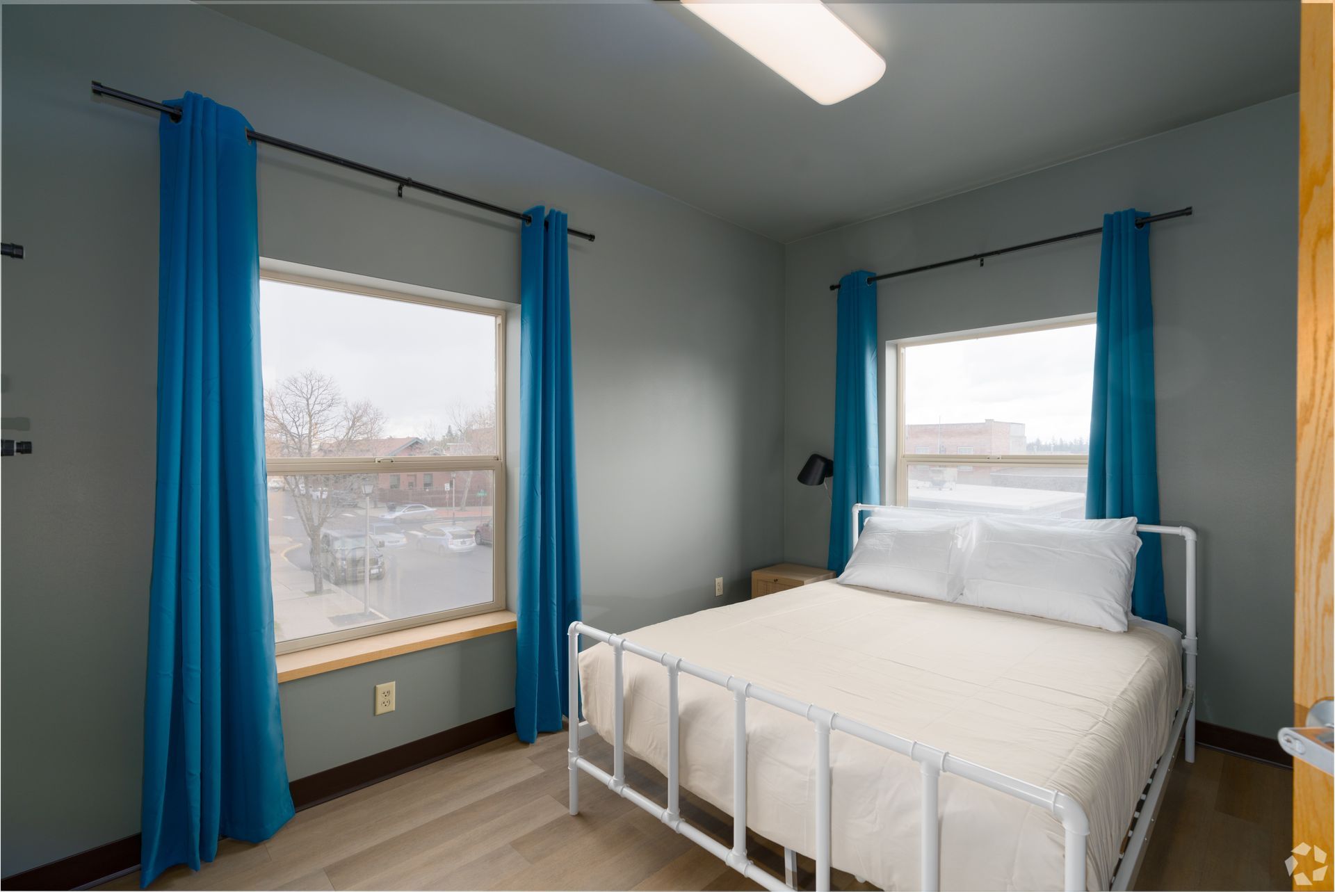 Bedroom with blue curtains, white bed frame, and two windows.
