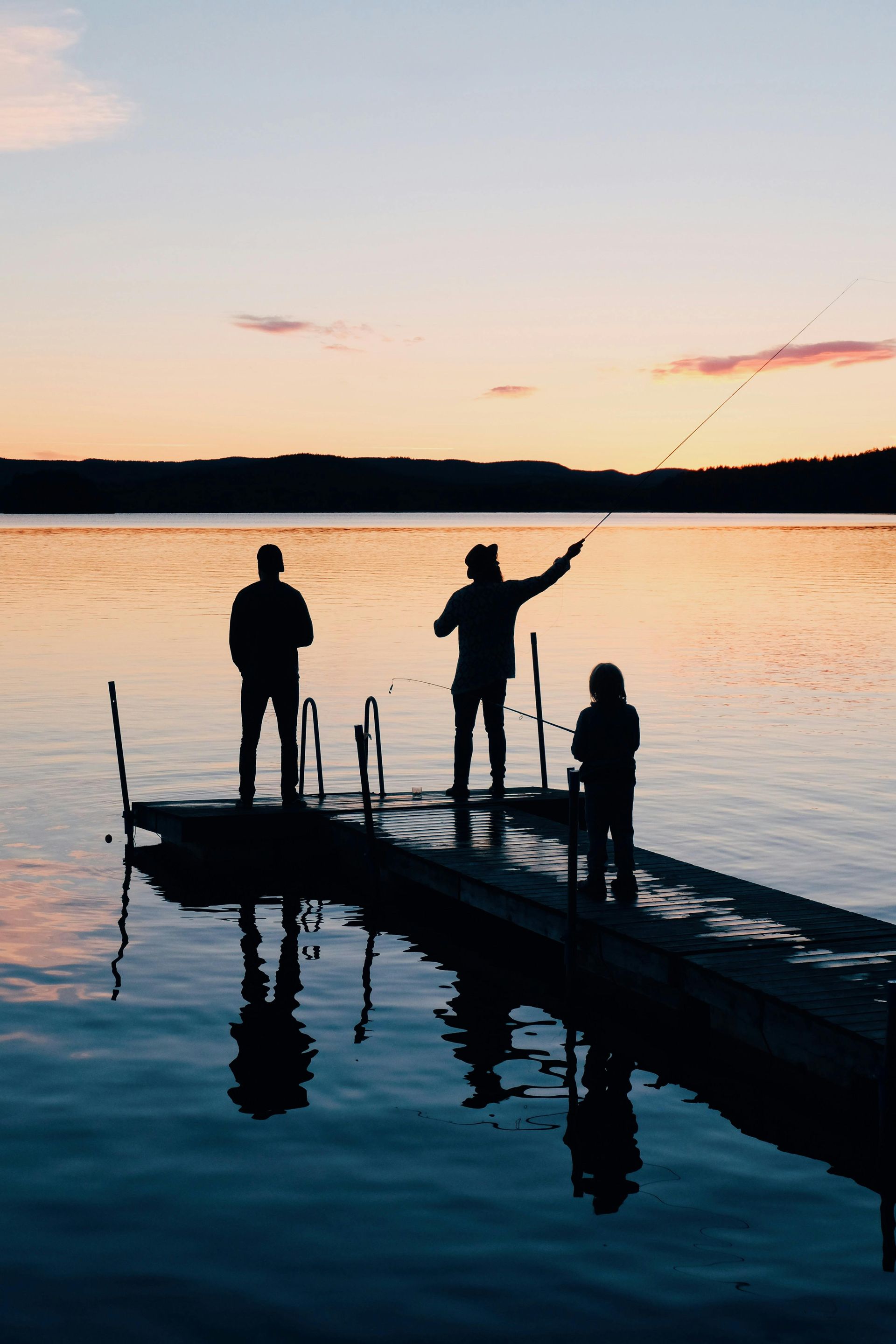 Silhouetted people fishing from a dock on a lake at sunset.