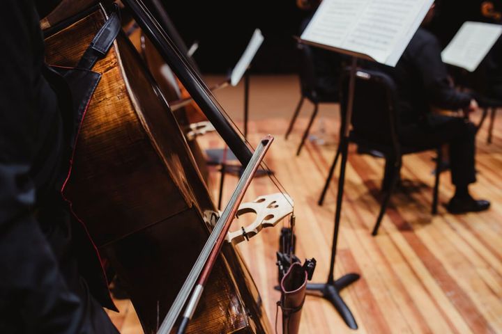 Cellos and music stands on a wooden stage in an orchestra rehearsal setting