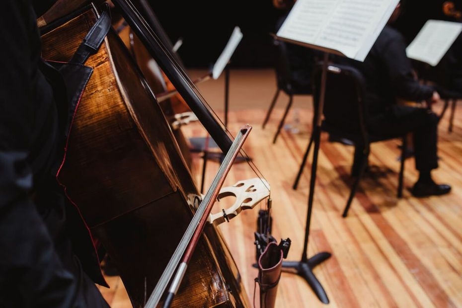 Cellos and music stands on a wooden stage in an orchestra rehearsal setting