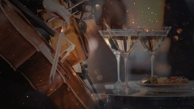 Three champagne glasses beside a violin and sheet music on a warmly lit table