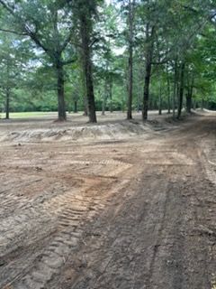 Dirt clearing with tire tracks among tall green trees in a park or wooded area