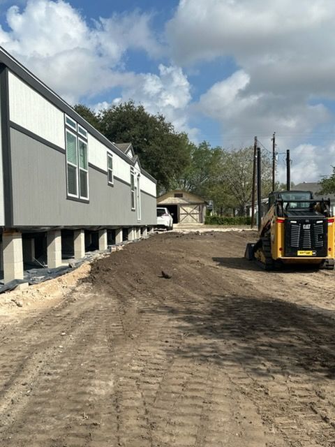 Construction site with modular building, dirt path, and a yellow skid steer under a partly cloudy sky