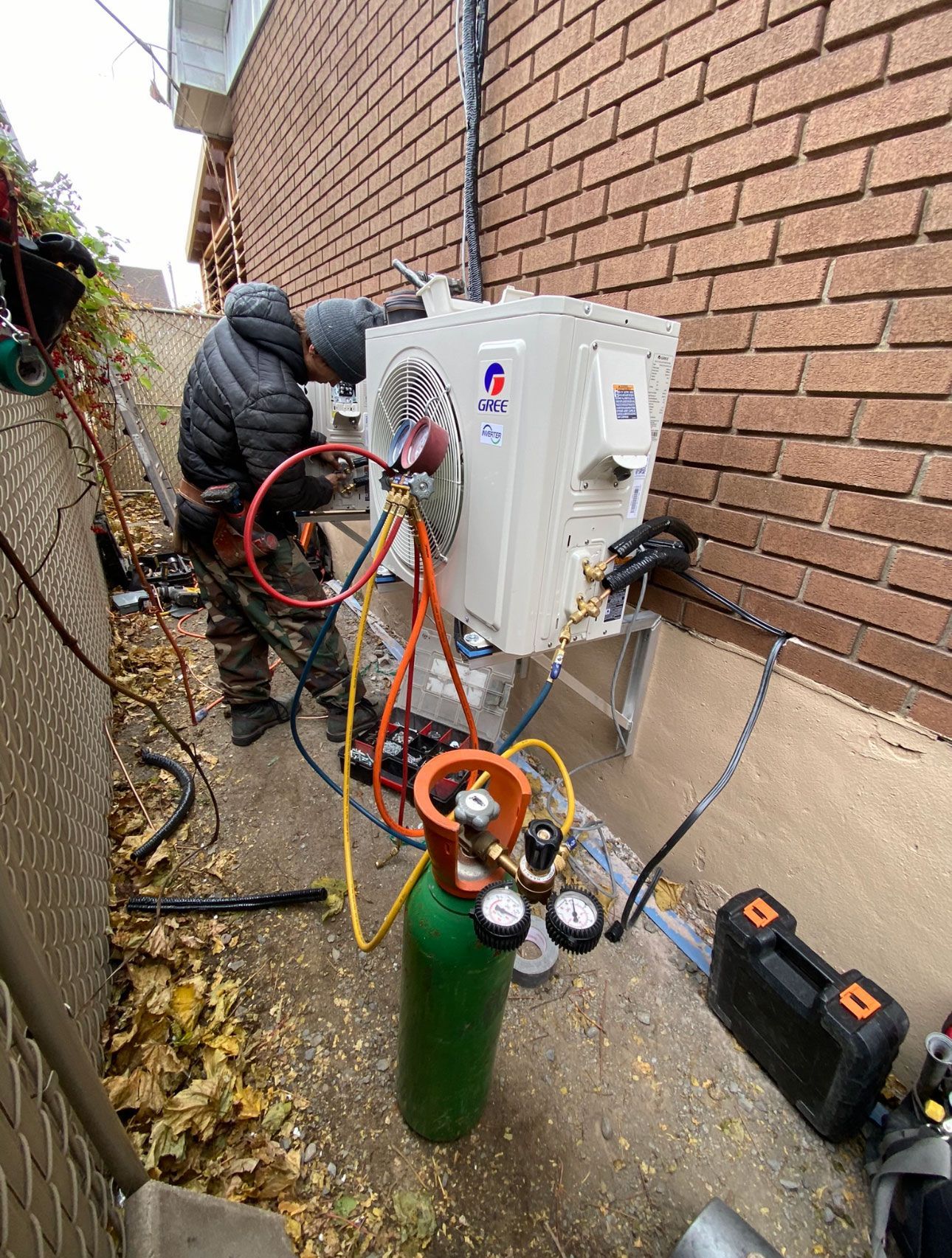 A man is installing an air conditioner on the side of a house.