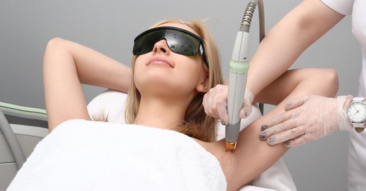 Women lying in body cover wearing laser eye protection glasses while the other woman doing her laser for underarms