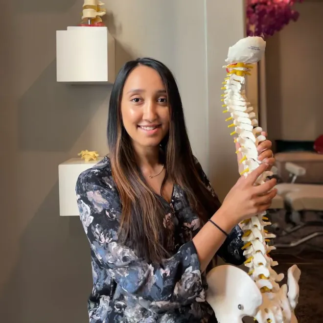 Woman smiling beside a human spine model in a clinic or classroom setting