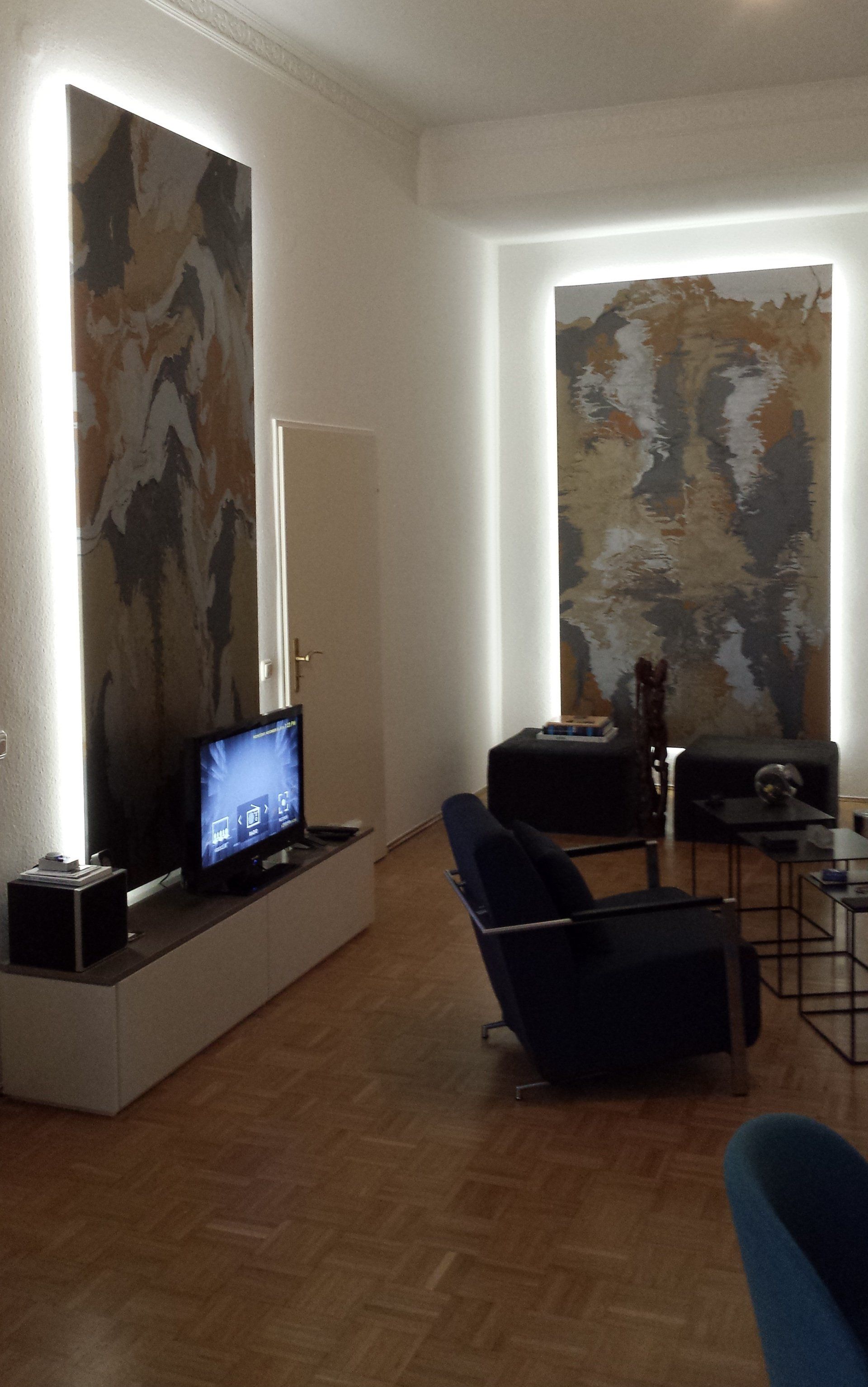 Schemerige woonkamer met abstracte muurkunst, tv op een tv-meubel en stoelen bij een staande lamp.