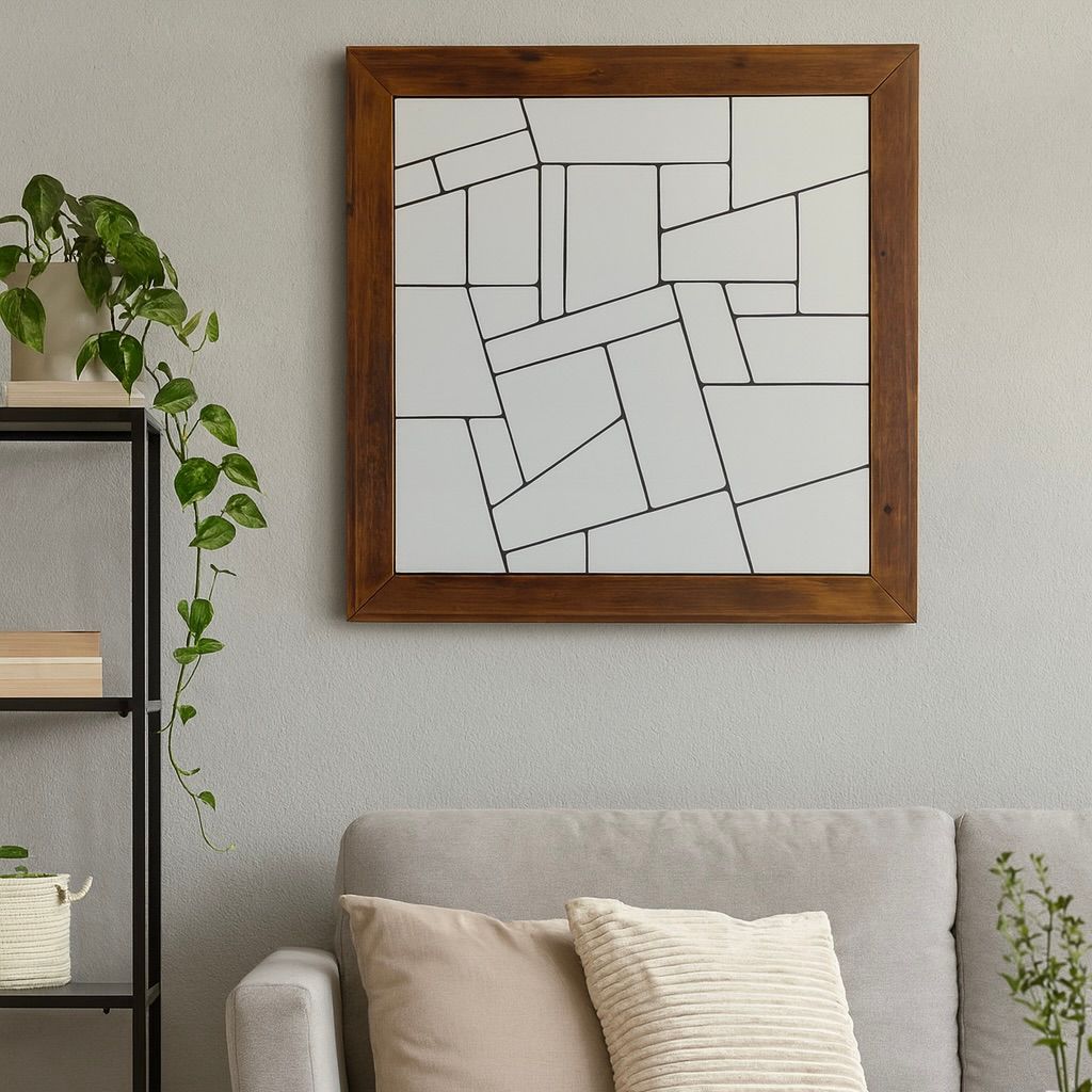 Ingelijste abstracte lijntekening aan een grijze muur boven een beige bank met kussens.