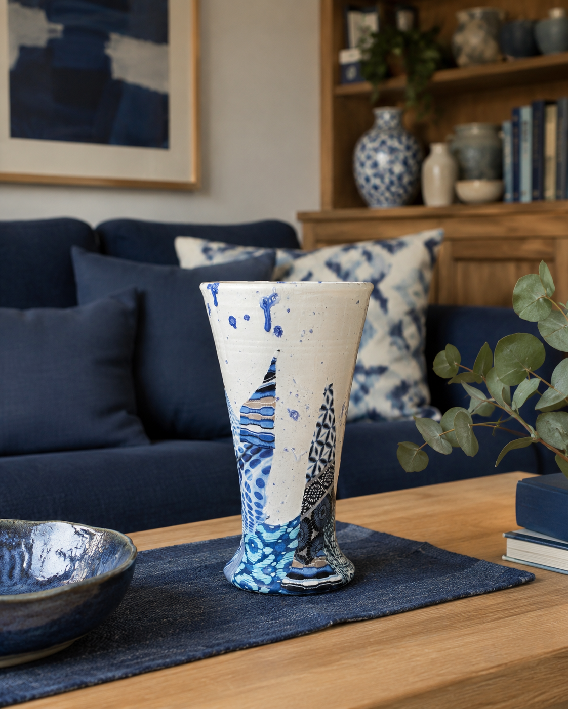 Een blauw-witte vaas op een salontafel in een gezellige woonkamer met een donkerblauwe bank en houten planken.