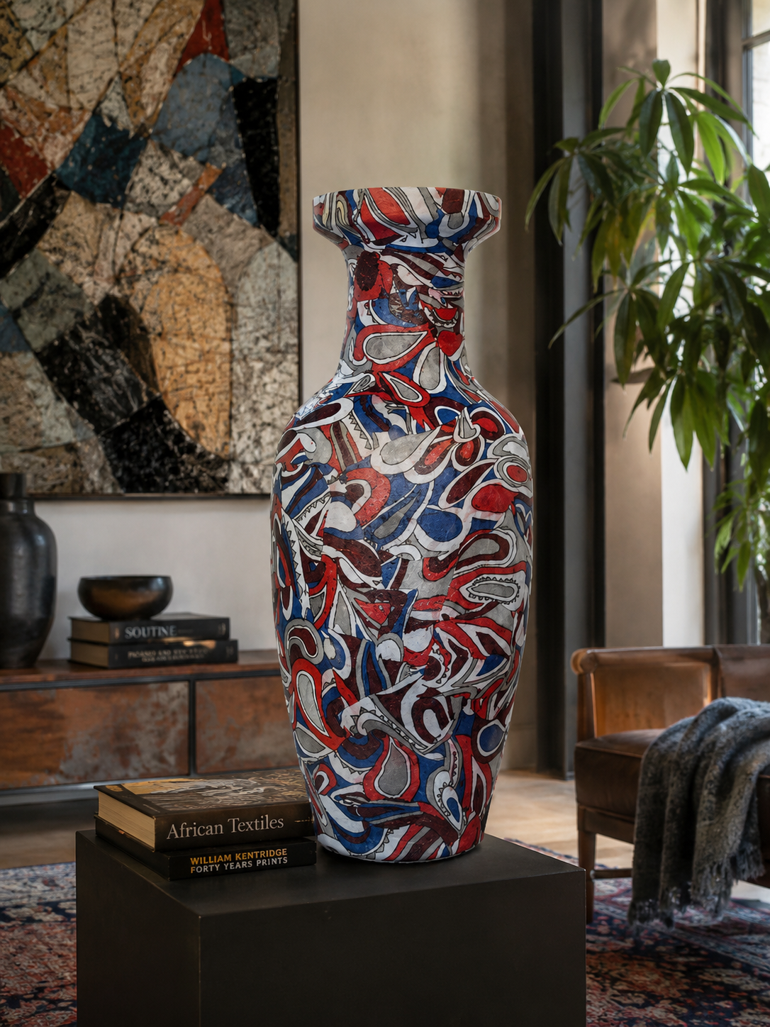 Een kleurrijke vaas met patroon op een zwarte sokkel in een moderne woonkamer met abstracte kunst en een plant.