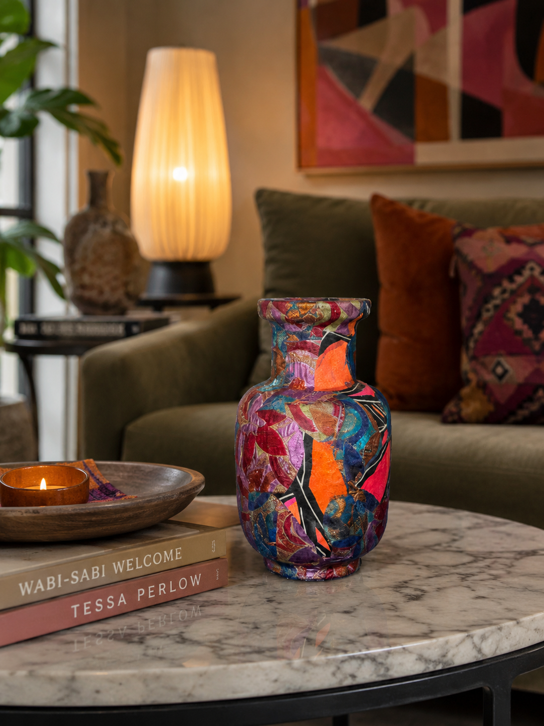 Een kleurrijke vaas met patroon op een marmeren tafel in een gezellige woonkamer met lamp en kussens.
