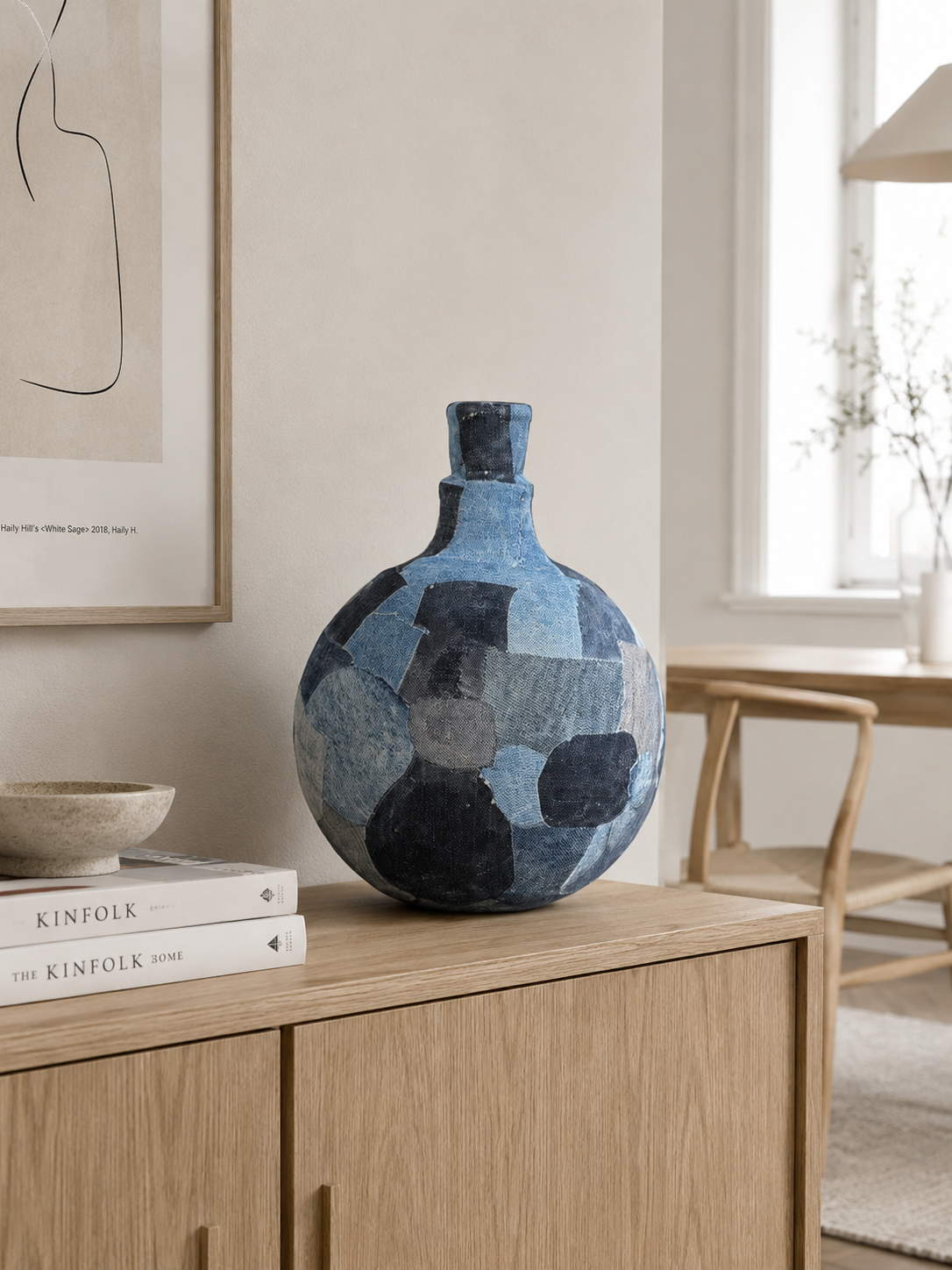 Blauwe vaas met patroon op een houten kast in een lichte, minimalistische kamer.