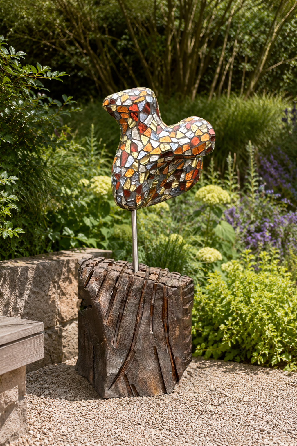 Mozaïekpaardsculptuur op een paal in een tuin naast een boomstronk en een grindpad.