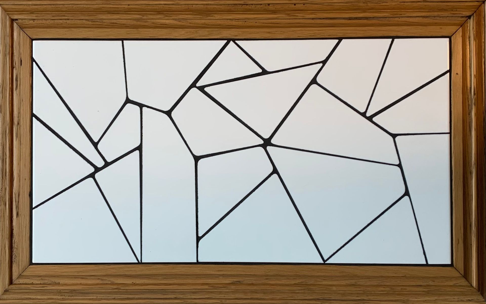 Abstracte geometrische kunst in een houten lijst met zwarte lijnen en lichtblauw-witte panelen.
