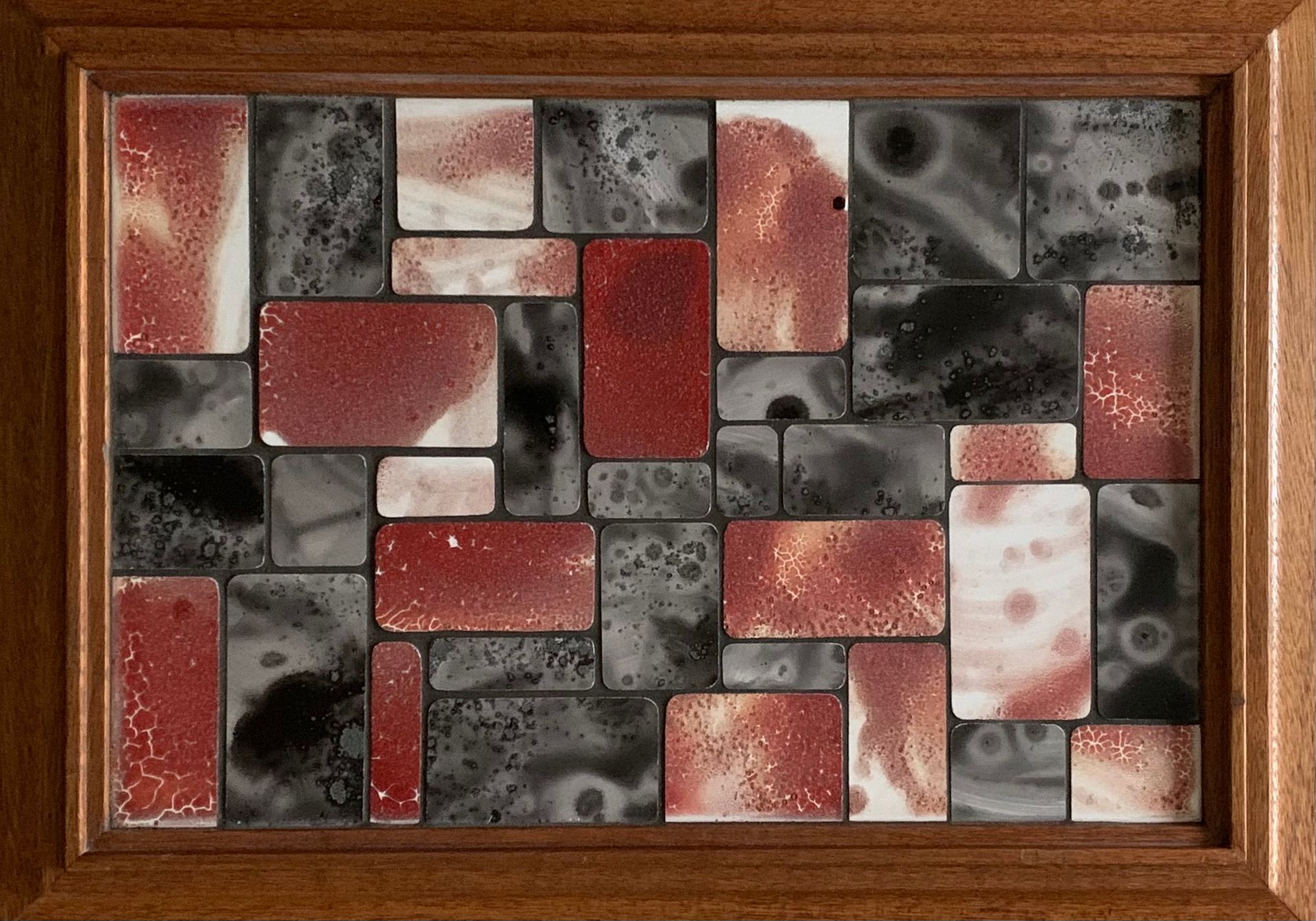 Abstracte mozaïek van rode, zwarte en witte rechthoekige tegels in een houten frame.