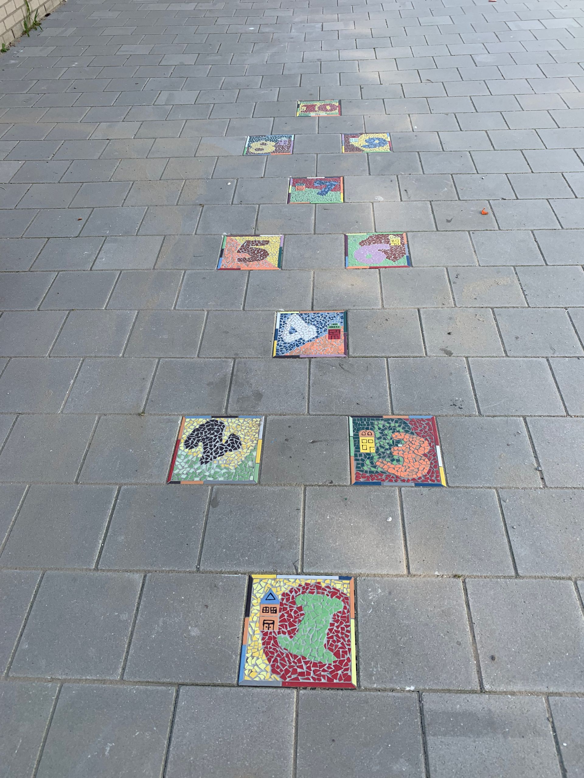 Kleurrijke vierkante kunstwerken, in een rij opgesteld op een grijze stenen bestrating.