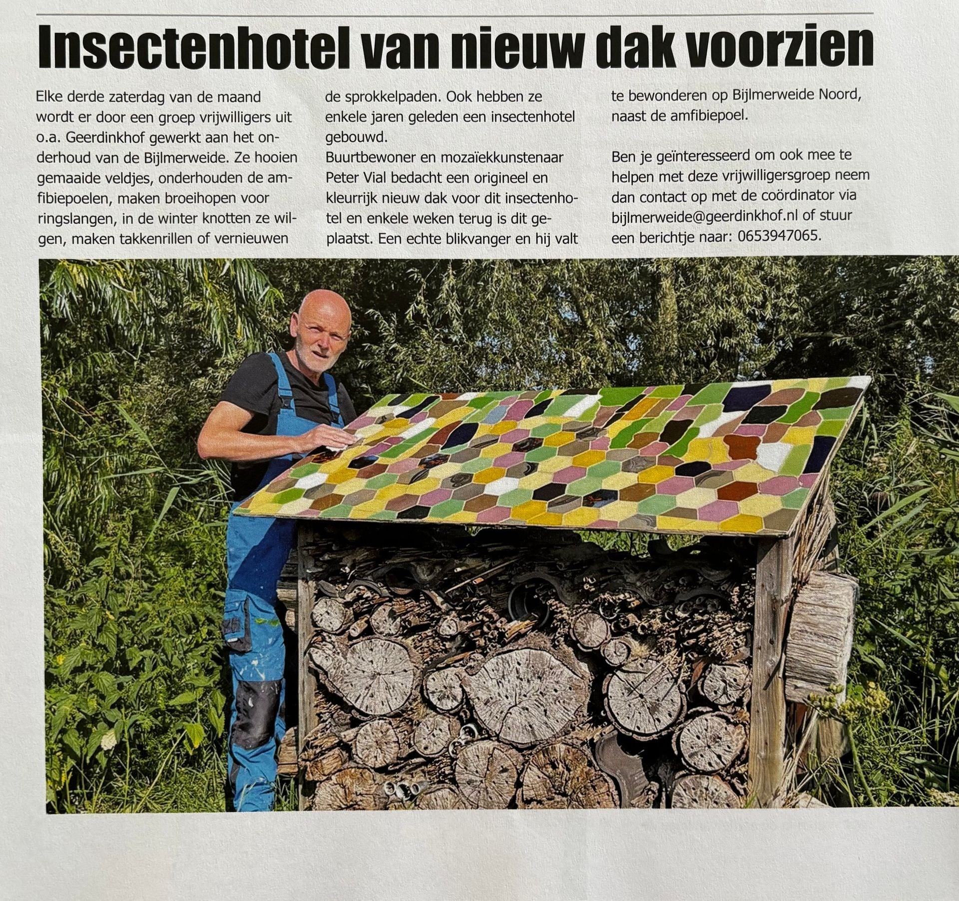 Een man plaatst een kleurrijk, gedessineerd dak op een groot insectenhotel in de buitenlucht.