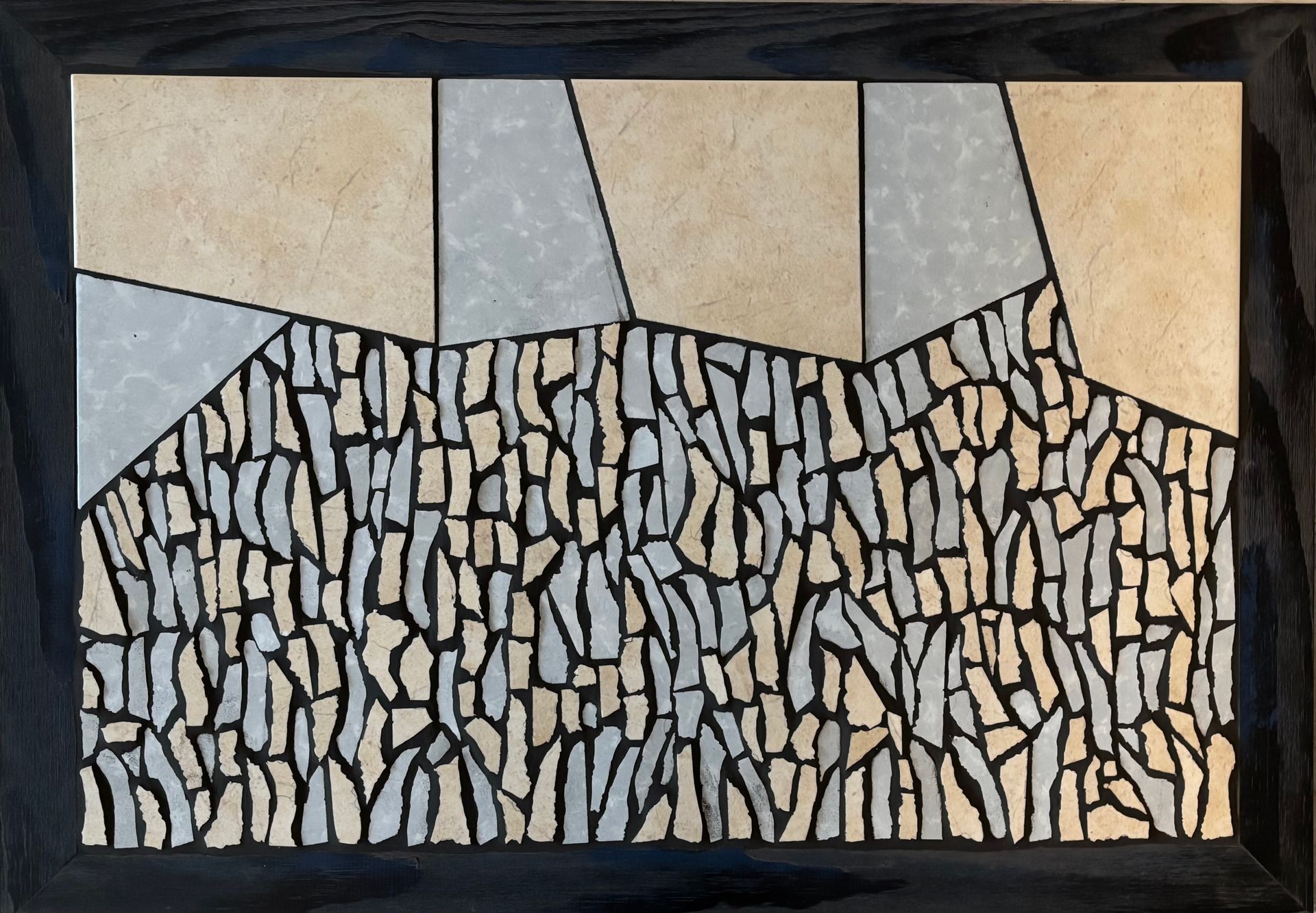 Abstracte mozaïek van beige, grijze en zwarte steenvormen in een ingelijst wandpaneel.