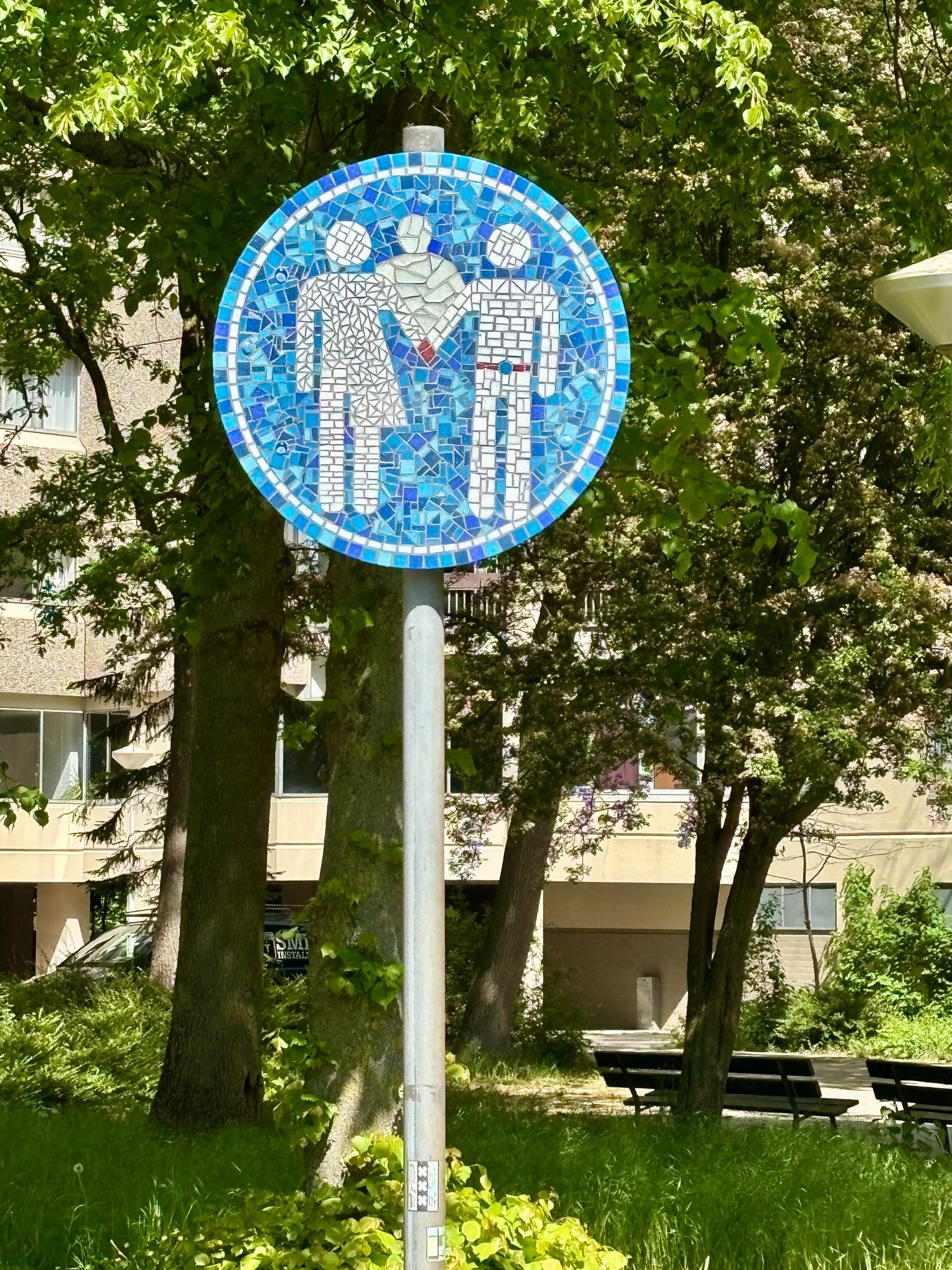 Blauw rond voetgangersbord op een paal in een groen park.