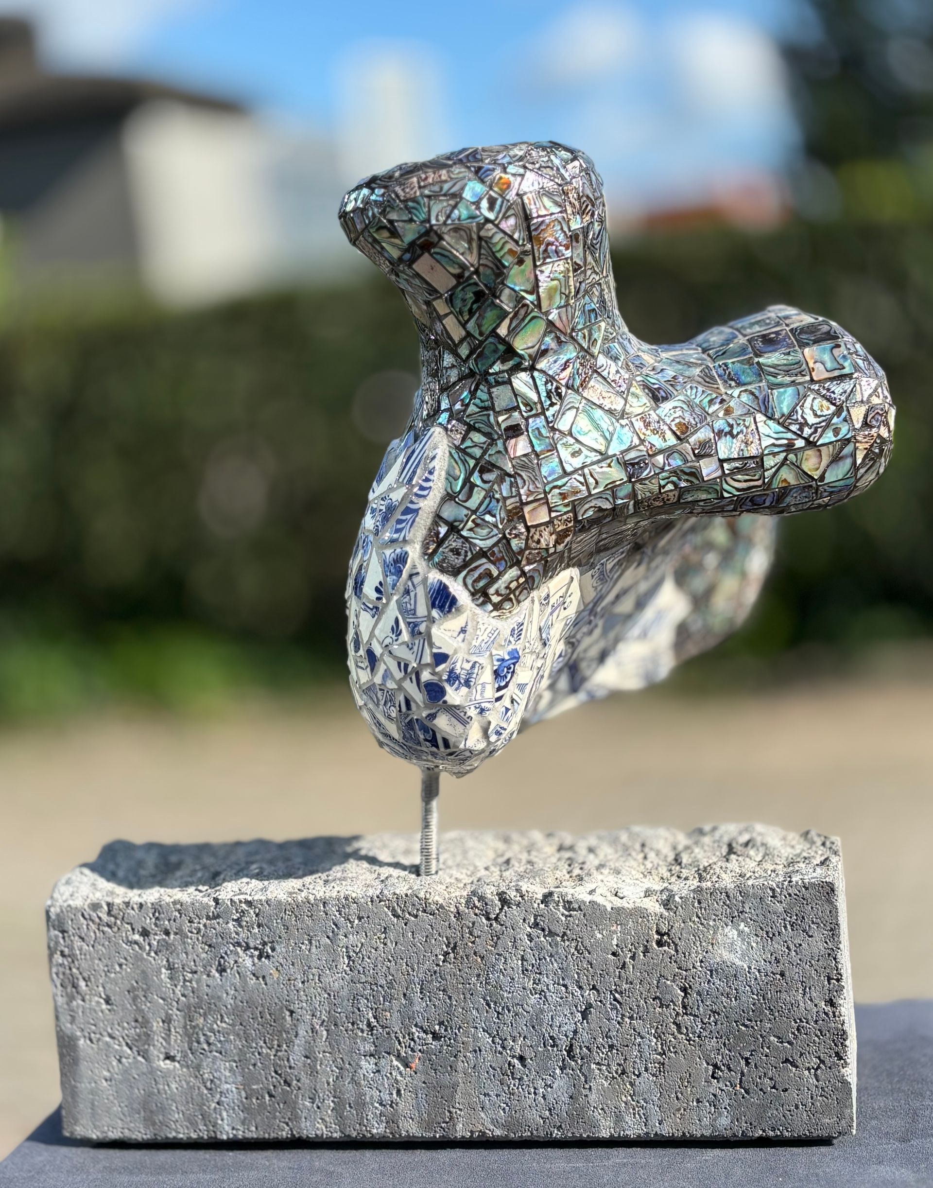 Abstracte metalen sculptuur, gemonteerd op een betonnen blok in de buitenlucht.