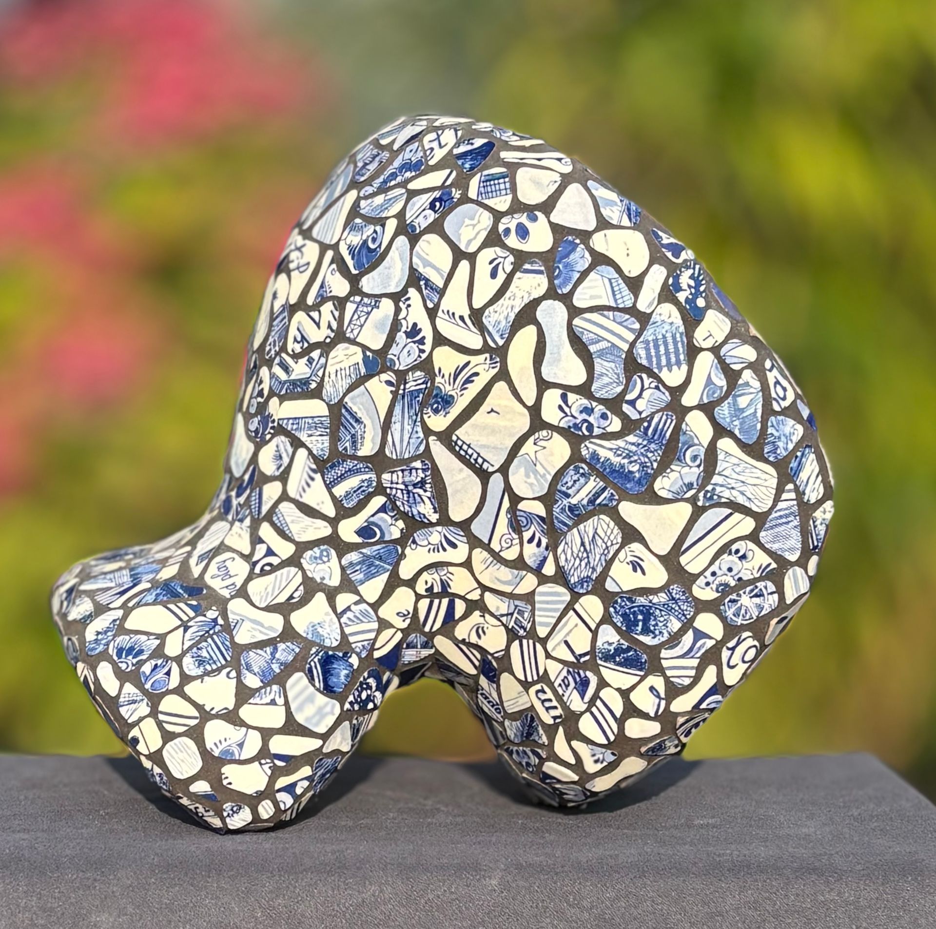 Abstracte mozaïeksculptuur met blauw-wit gedecoreerde stenen op een grijze ondergrond.