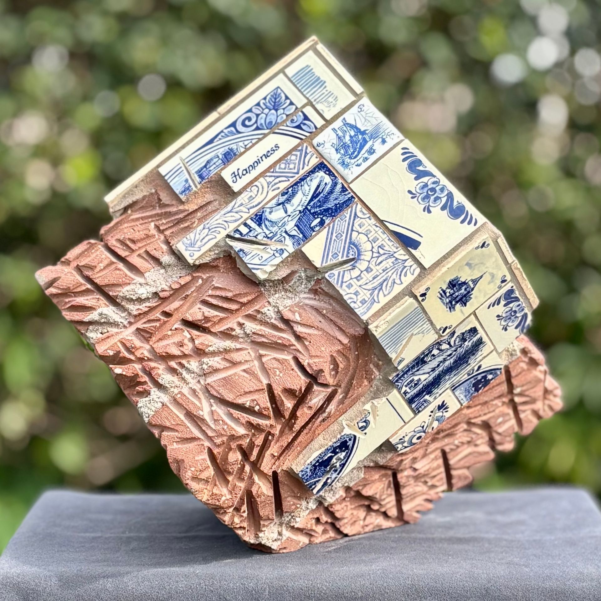 Abstracte geometrische kubussculptuur met blauw-crèmekleurige tegels op een grijze sokkel.