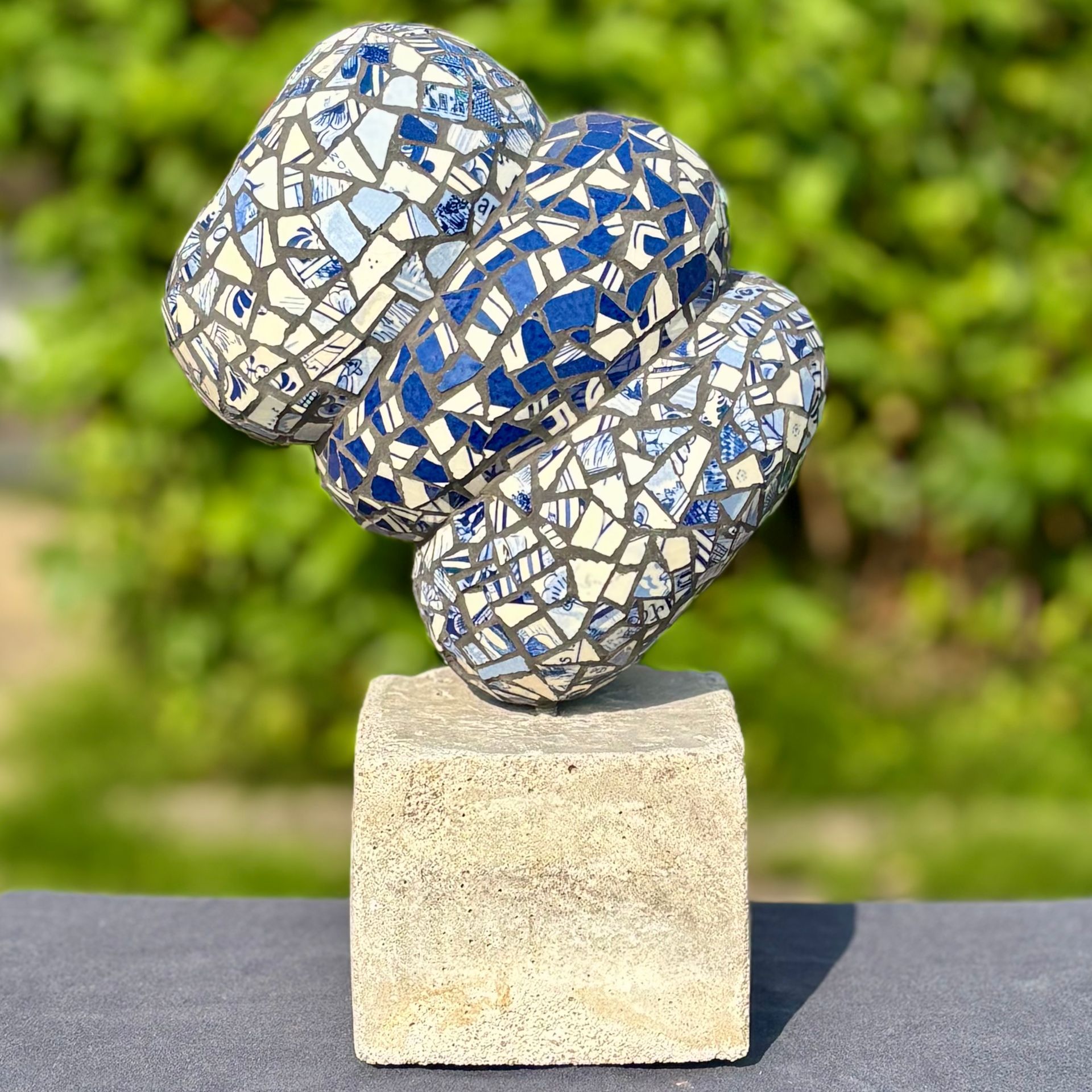 Abstracte mozaïeksculptuur van drie zilveren en blauwe ronde vormen op een stenen sokkel in de buitenlucht.